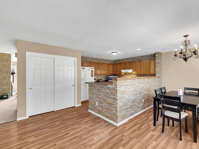 kitchen featuring white refrigerator with ice dispenser, a notable chandelier, light wood-style floors, and a peninsula
