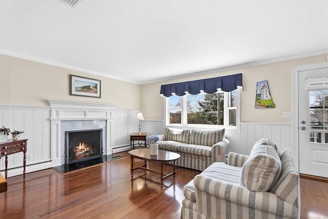 living room featuring wainscoting, wood finished floors, a baseboard radiator, and crown molding