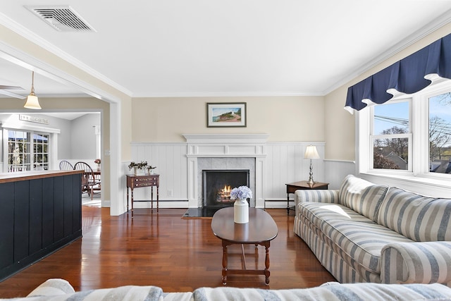 living area with baseboard heating, a baseboard heating unit, wainscoting, and visible vents