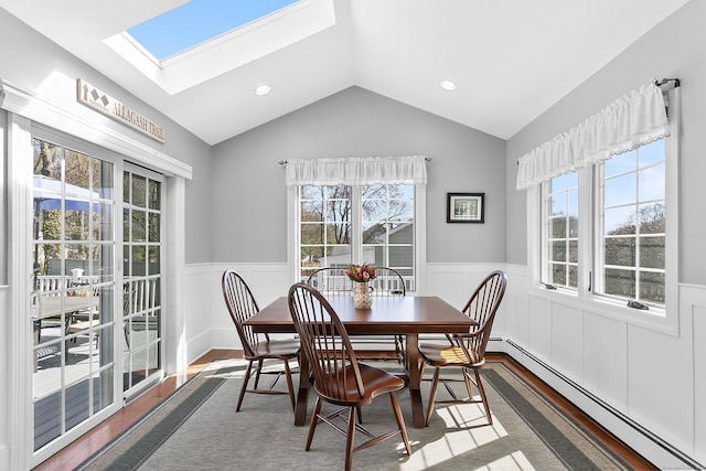 dining area featuring baseboard heating, vaulted ceiling with skylight, wainscoting, and wood finished floors