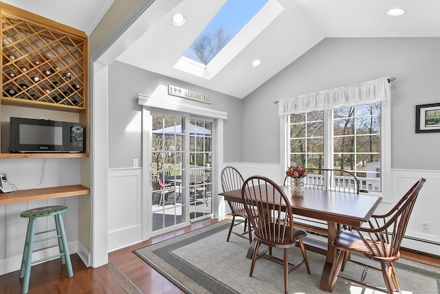 dining room featuring vaulted ceiling with skylight, wood finished floors, a wealth of natural light, and wainscoting
