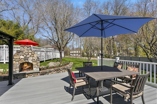wooden terrace featuring fence, an outdoor stone fireplace, outdoor dining area, and a yard