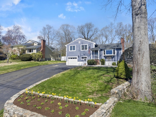 split level home with a chimney, a front lawn, driveway, and a garage