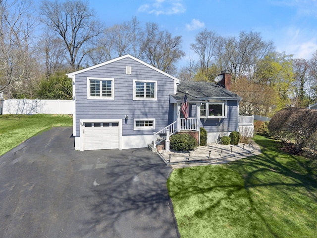 split level home featuring a chimney, fence, driveway, a front yard, and a garage
