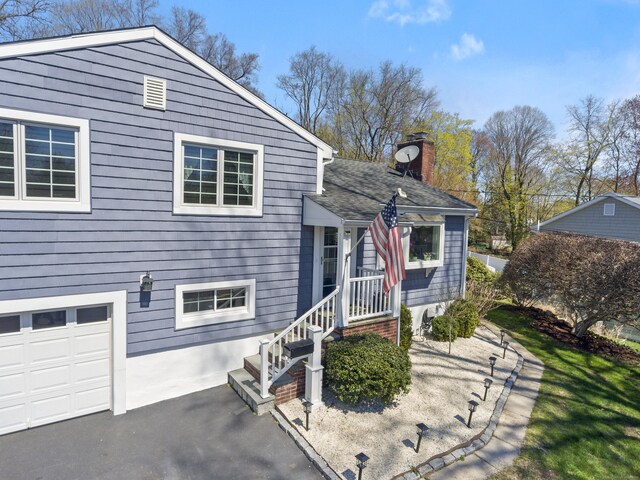 split level home featuring a chimney, driveway, a shingled roof, and a garage