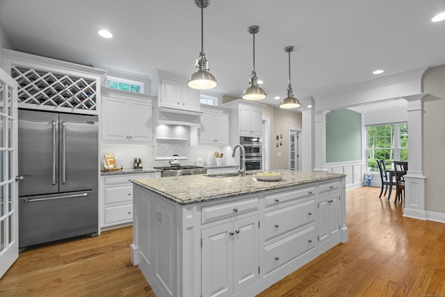 301 Fox Hopyard Rd, East Haddam, CT 06423 - kitchen with appliances with stainless steel finishes, decorative columns, white cabinetry, a kitchen island with sink, and light wood-type flooring
