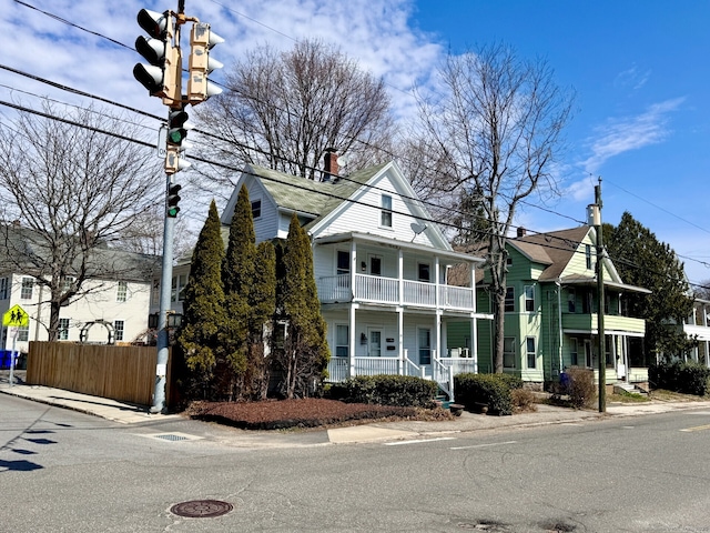 view of front of home with covered porch, a balcony, fence, and a chimney
