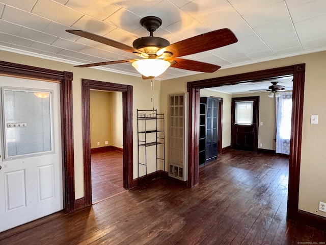 empty room featuring ornamental molding, dark wood-type flooring, baseboards, and ceiling fan