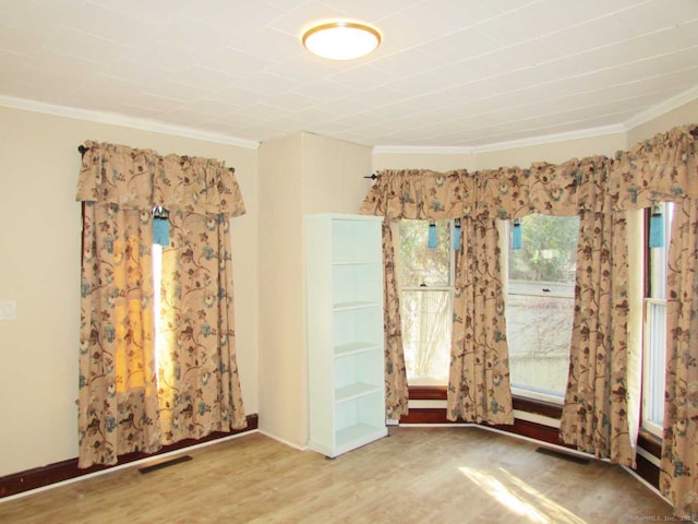 empty room featuring baseboards, visible vents, crown molding, and wood finished floors