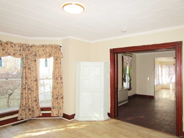 spare room featuring baseboards, visible vents, wood finished floors, and ornamental molding
