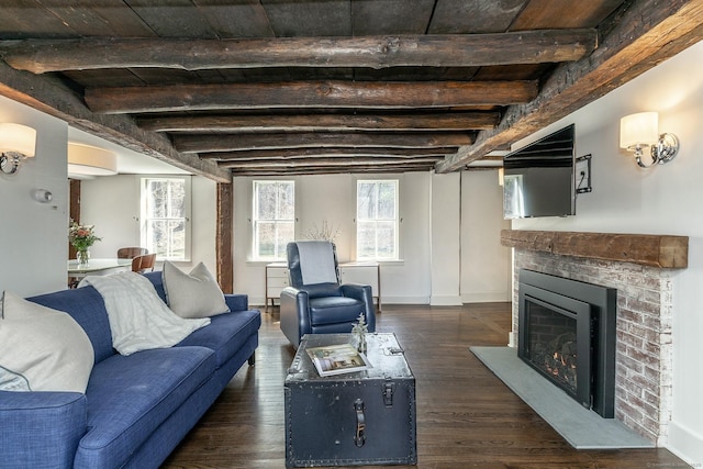 living room with beamed ceiling, baseboards, dark wood finished floors, and a warm lit fireplace