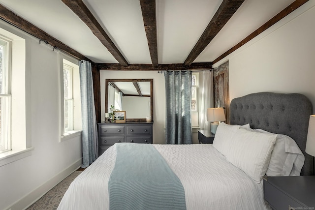 bedroom featuring beamed ceiling, baseboards, multiple windows, and carpet floors