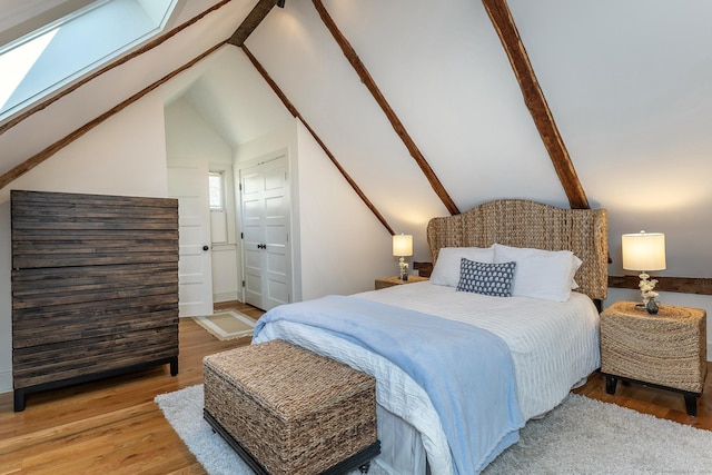 bedroom featuring vaulted ceiling with skylight, baseboards, and wood finished floors
