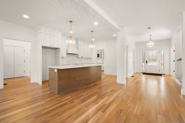 kitchen with light countertops, baseboards, white cabinets, light wood-style flooring, and an island with sink