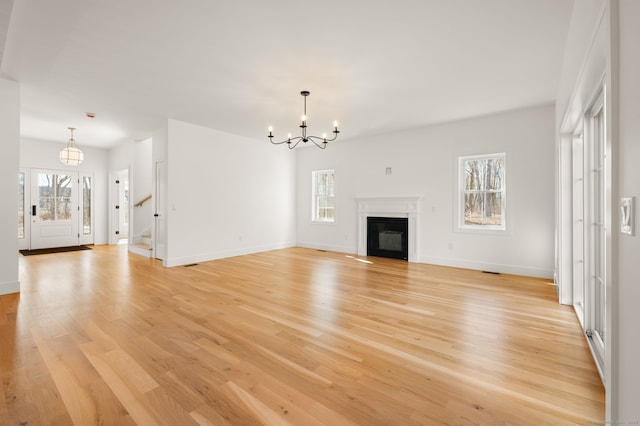 unfurnished living room featuring baseboards, an inviting chandelier, plenty of natural light, and light wood-style floors