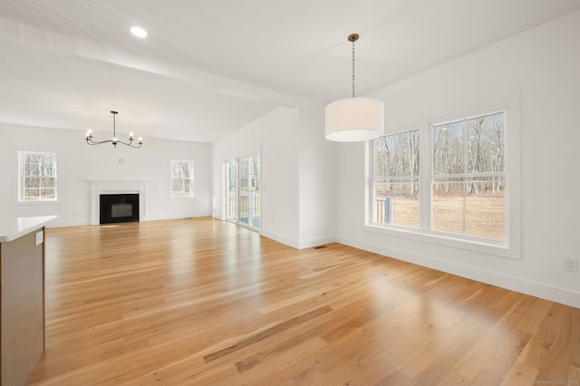 unfurnished living room featuring baseboards, a chandelier, a wealth of natural light, and light wood-type flooring