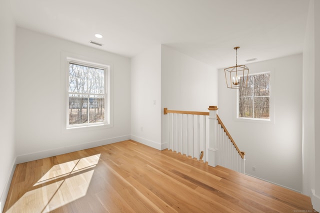 spare room featuring visible vents, light wood-style floors, plenty of natural light, and a chandelier