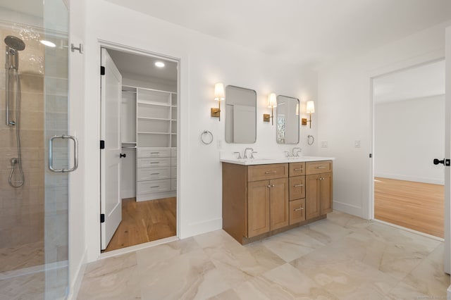 bathroom with double vanity, a walk in closet, a stall shower, a sink, and marble finish floor