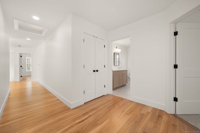 hallway featuring light wood-style floors, attic access, and baseboards