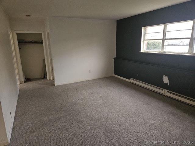 unfurnished bedroom with a closet, carpet floors, and a baseboard heating unit