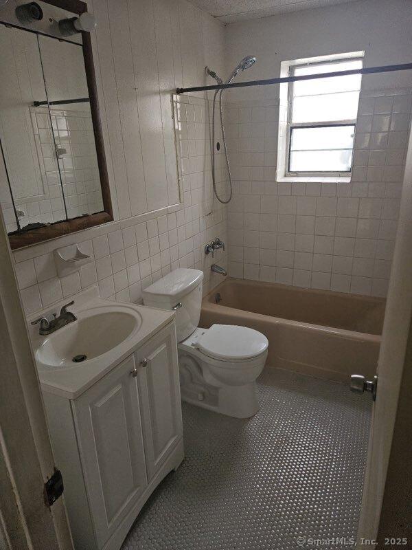 full bathroom featuring vanity, tile walls, toilet, tile patterned floors, and  shower combination