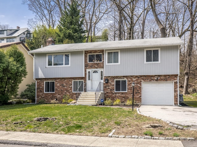 bi-level home with driveway, a chimney, brick siding, an attached garage, and a front yard