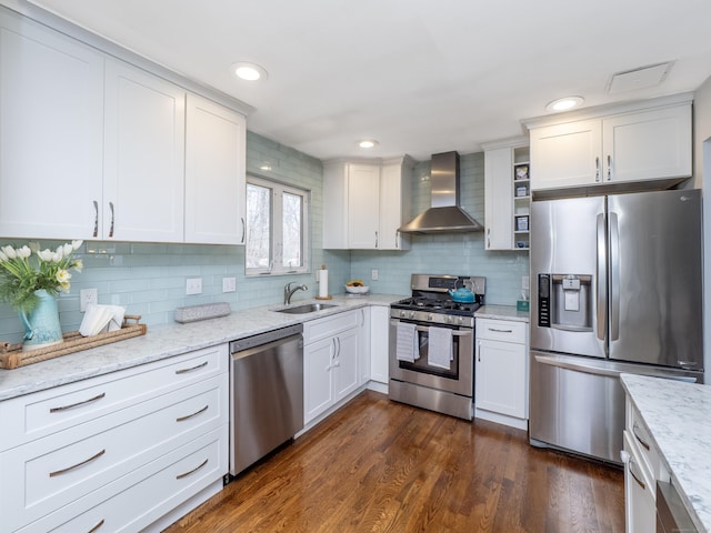 kitchen featuring a sink, wall chimney exhaust hood, tasteful backsplash, appliances with stainless steel finishes, and white cabinetry