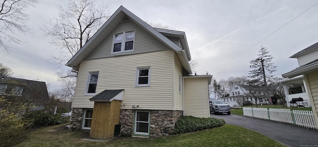 rear view of house featuring fence, driveway, stone siding, and a yard