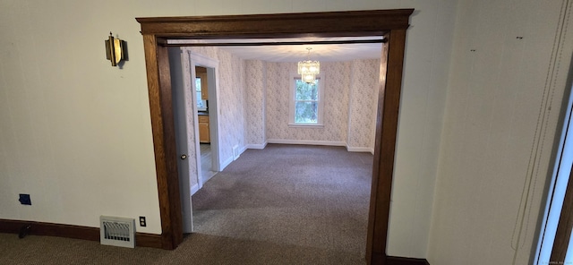 hallway featuring baseboards, carpet floors, visible vents, and an inviting chandelier
