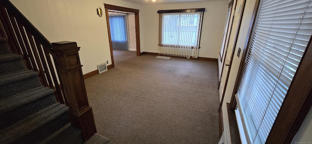 carpeted empty room with baseboards, visible vents, radiator heating unit, and stairway