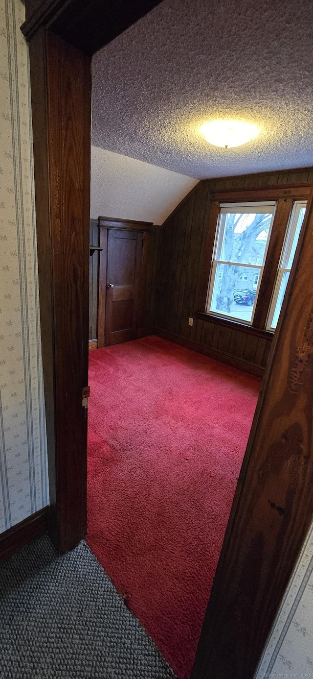 bonus room with lofted ceiling, light colored carpet, baseboards, a textured ceiling, and wallpapered walls