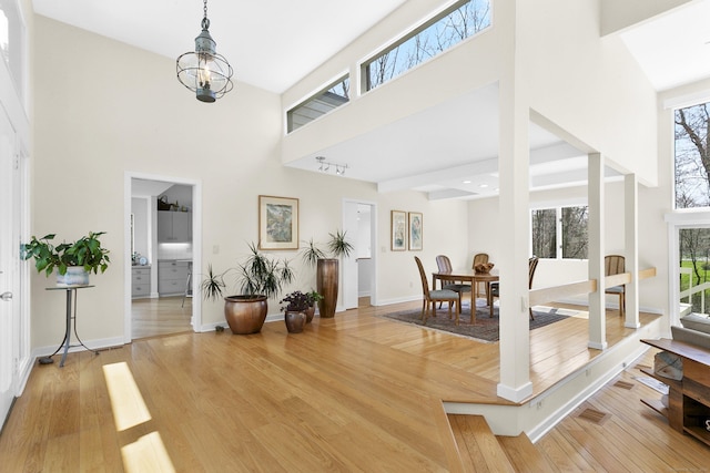 entryway with baseboards, a towering ceiling, an inviting chandelier, and light wood-style floors