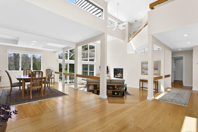 living room featuring baseboards, a high ceiling, a ceiling fan, light wood-style flooring, and a glass covered fireplace