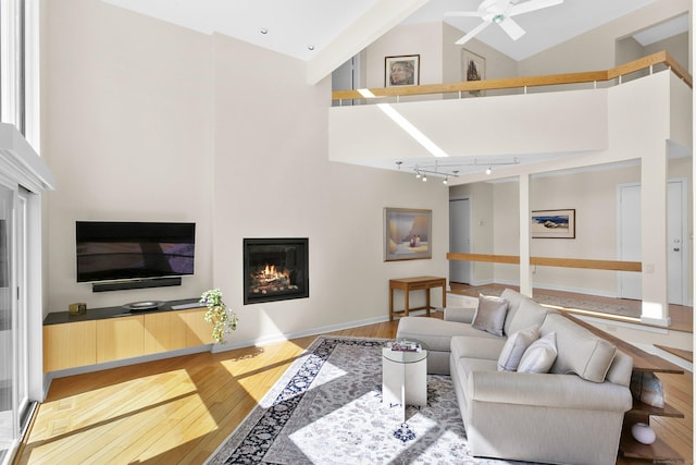 living room with rail lighting, wood finished floors, high vaulted ceiling, and a glass covered fireplace