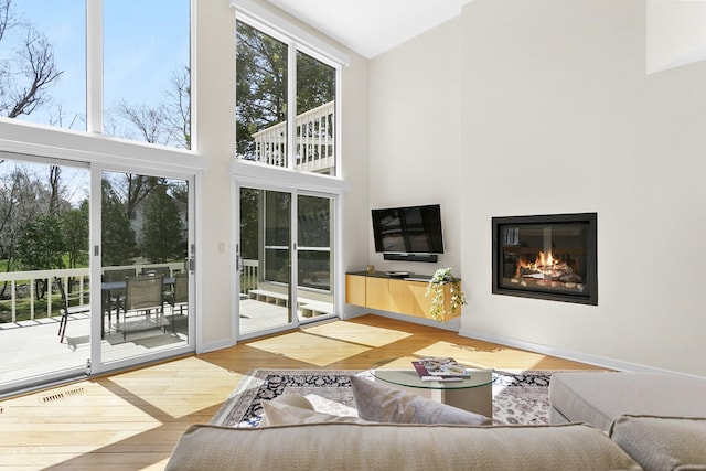 living room with a high ceiling, wood finished floors, a glass covered fireplace, and visible vents