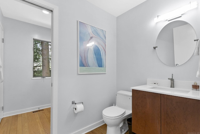 half bathroom with visible vents, baseboards, toilet, vanity, and wood finished floors