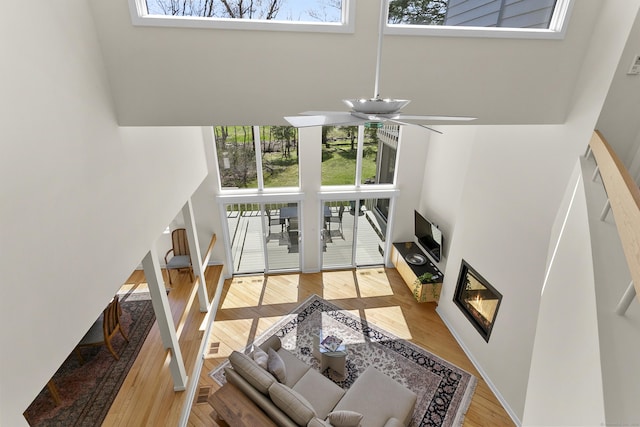 living area with a glass covered fireplace, wood finished floors, a healthy amount of sunlight, and a towering ceiling