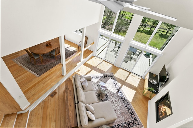 living area featuring a glass covered fireplace, wood finished floors, a high ceiling, and ceiling fan
