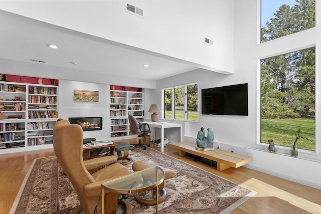 living area featuring visible vents, a glass covered fireplace, and wood finished floors