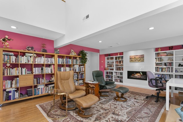 living area featuring wall of books, recessed lighting, wood finished floors, visible vents, and a lit fireplace