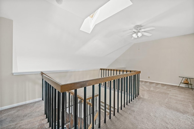 interior space featuring carpet flooring, baseboards, a ceiling fan, and vaulted ceiling with skylight