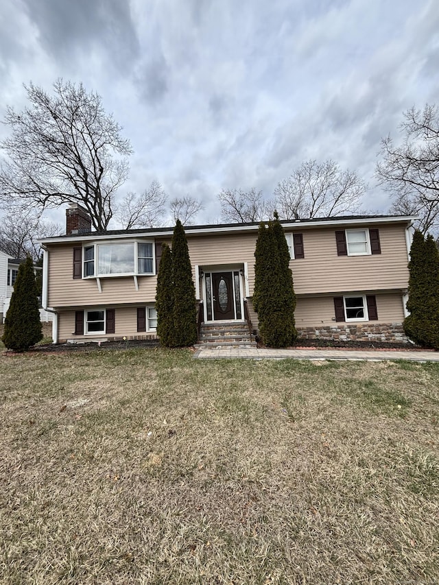 bi-level home featuring entry steps, a chimney, and a front yard