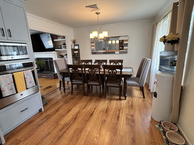 dining space with an inviting chandelier, light wood-style flooring, ornamental molding, a fireplace with raised hearth, and visible vents