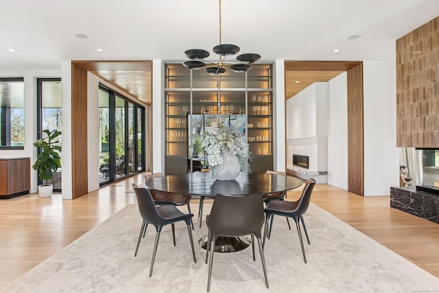 dining space featuring a fireplace, light wood-style flooring, a chandelier, built in shelves, and recessed lighting
