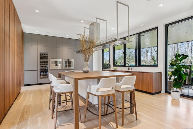 kitchen with modern cabinets, light wood-style flooring, butcher block countertops, a center island, and a kitchen breakfast bar