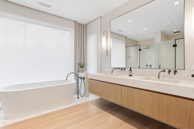 full bathroom with a stall shower, a soaking tub, double vanity, wood finished floors, and recessed lighting