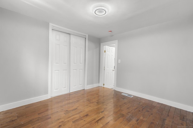 unfurnished bedroom with baseboards, a closet, wood finished floors, and visible vents