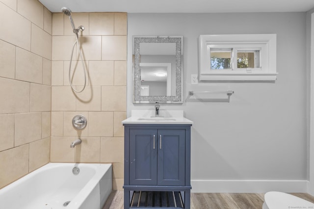 full bathroom featuring vanity, wood finished floors, toilet, baseboards, and washtub / shower combination