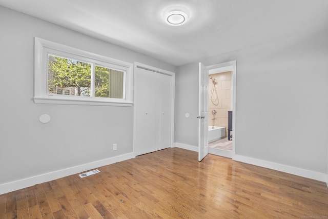 unfurnished bedroom featuring visible vents, a closet, wood finished floors, baseboards, and connected bathroom