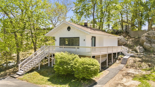 view of front of house with a chimney, roof with shingles, stairway, and a deck
